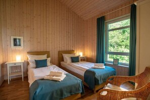 Ein Zimmer mit zwei Betten, einem Korbsessel und einem Fenster mit Vorhängen.