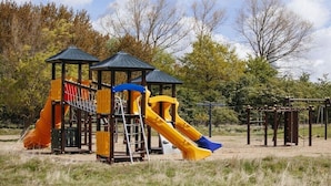 A playground with slides and climbing structures, surrounded by trees. - Pilot station type G (Neustadt\/Holstein - OT Pelzerhaken)
