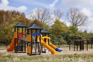 Ein Spielplatz mit Rutschen und Klettergerüsten, umgeben von Bäumen.