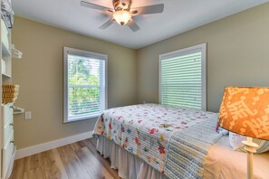 A bedroom with a bed, a ceiling fan, two windows with blinds, a lamp, and a wooden floor. - Canal-Front Gem w/ Dock & Guest Home in Cortez! (Cortez)
