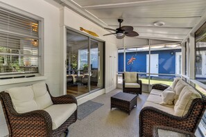 Una veranda coperta con mobili in vimini, una ventola a soffitto e vista su un edificio blu.