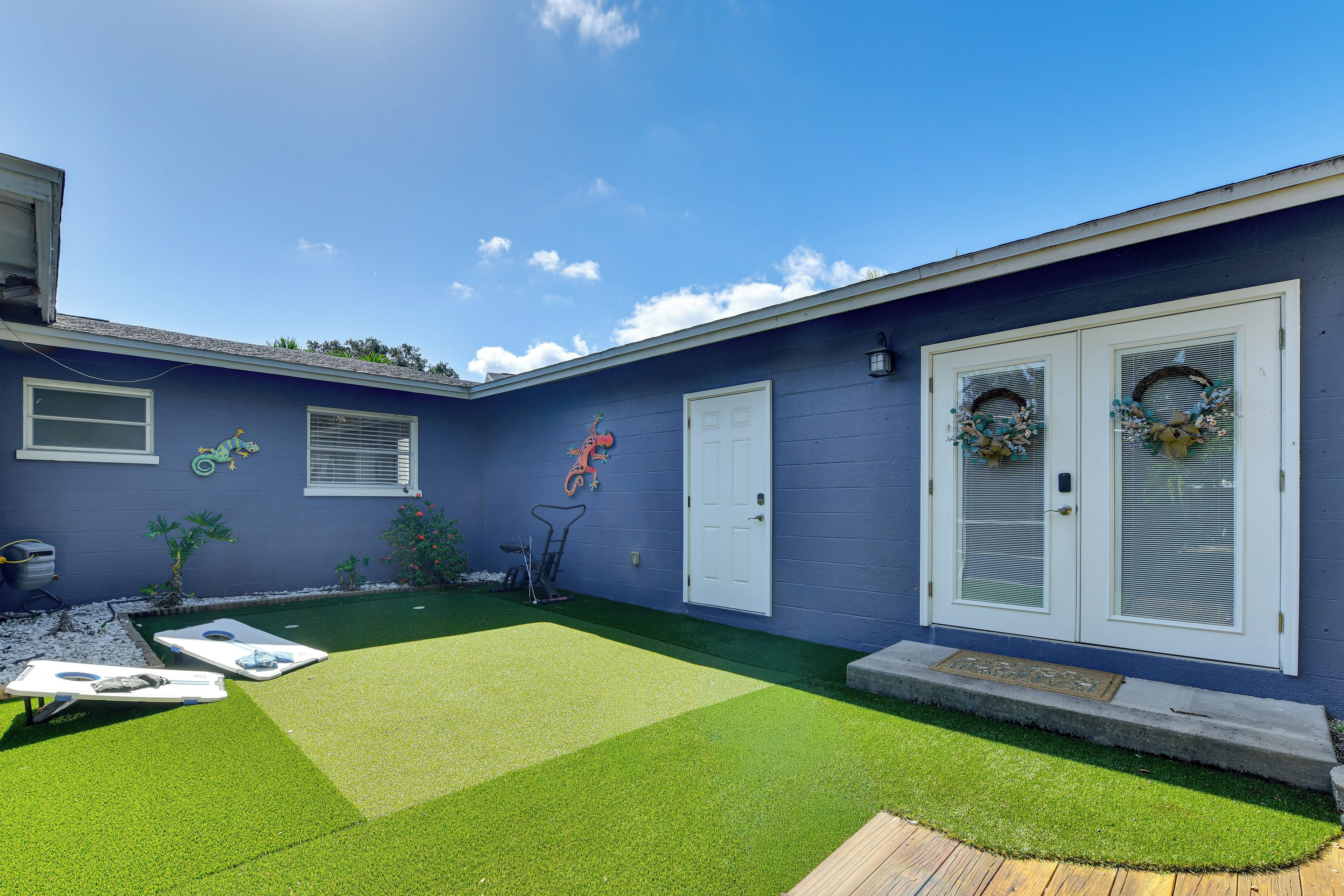 Un edificio residenziale con facciata blu, una porta bianca, un piccolo giardino con erba sintetica e un patio in legno.