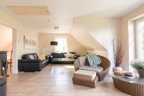 Ein geräumiges Wohnzimmer mit einem schwarzen Ledersofa, einem Korbsessel und einem Glastisch.