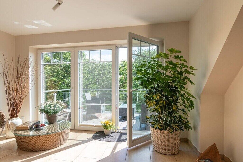 Una habitación luminosa con ventanas amplias, un sofá de mimbre y una planta en maceta.