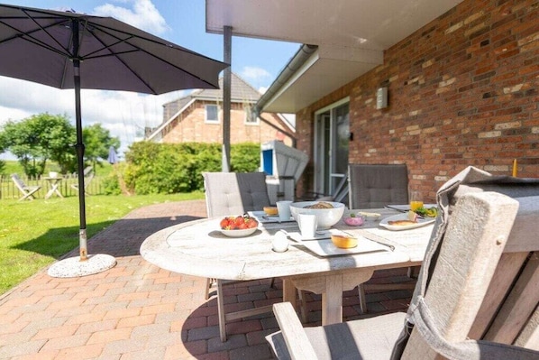 Eine Außenpatio mit einem runden Tisch, Stühlen und einem großen Sonnenschirm.