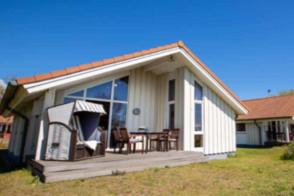A single-story building with a sloped roof, large windows, and a porch with chairs.