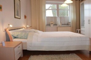 Een slaapkamer met een bed, nachtkastje, lamp, raam met gordijnen en een radiator.