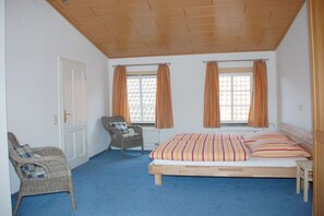 Une chambre avec un lit simple, deux fenêtres avec des rideaux, une chaise et un radiateur.