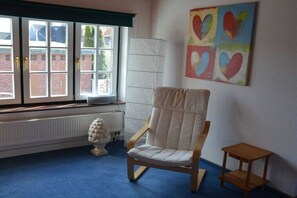 A room with a large window, a chair, a small table, and a colorful heart-themed artwork on the wall. - Holiday apartment with 1 bedroom (Husum\/ Nordsee)