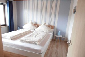 Quarto com cama, almofadas, mesa de cabeceira e janela com cortinas.