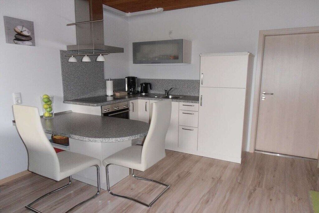 A compact kitchen with a central island, two white chairs, a coffee maker, and a refrigerator.