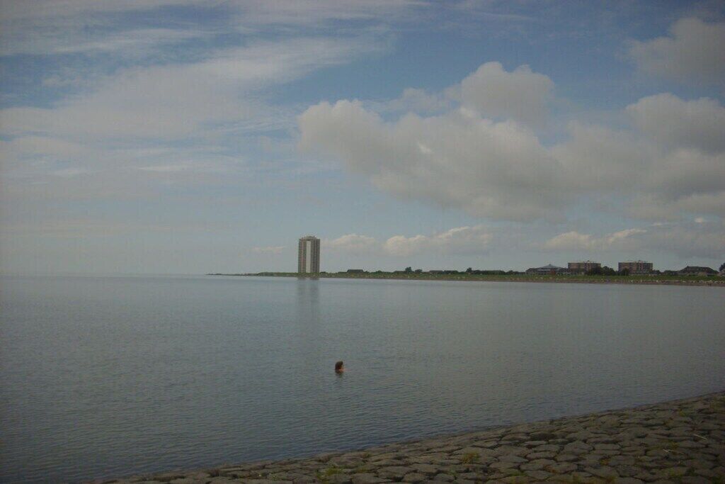 A calm body of water with a distant building and a clear sky.