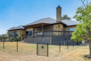 Ein zweistöckiges Steinhaus mit Metalldach, einer überdachten Terrasse und einem eingezäunten Garten.