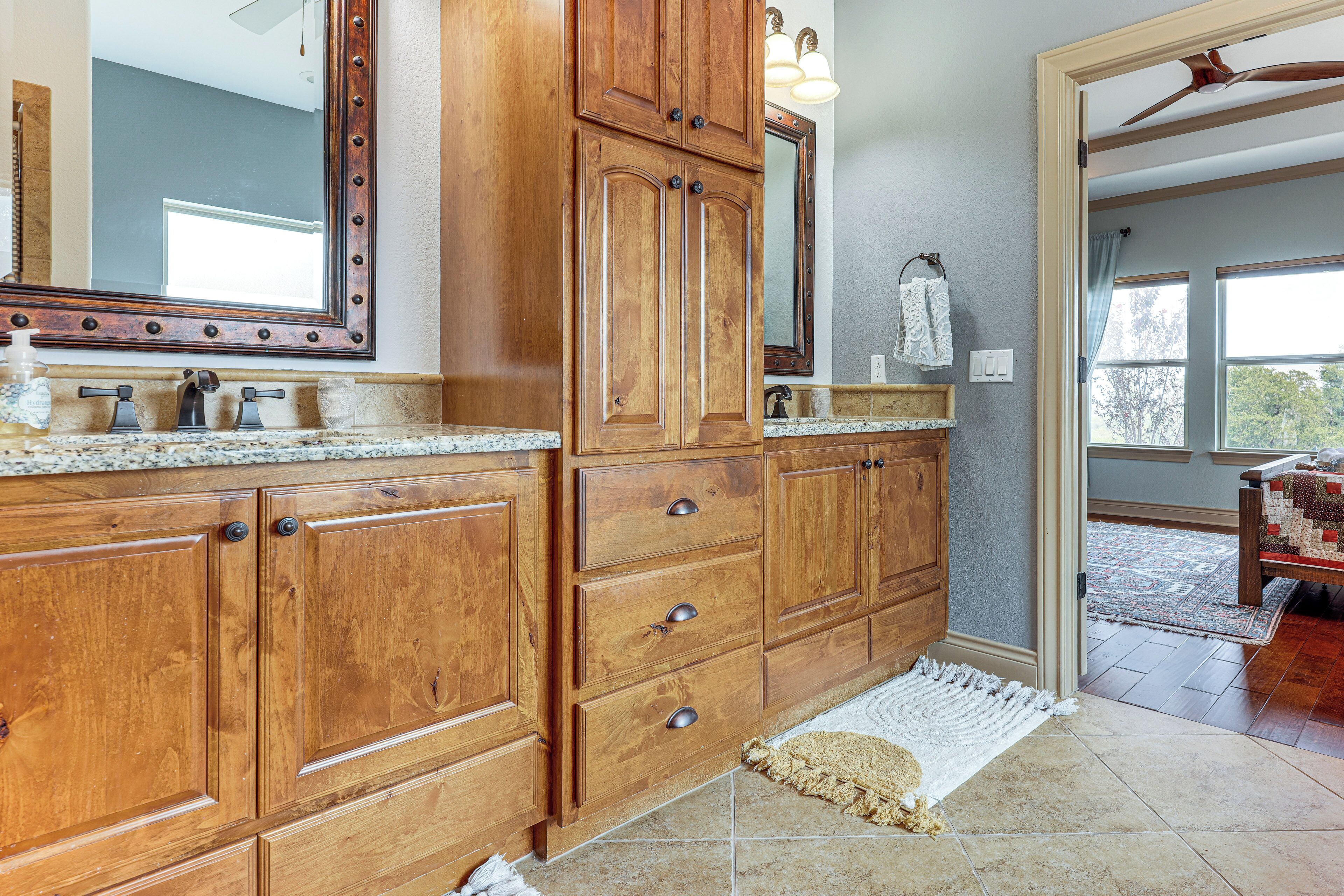 A bathroom with wooden cabinetry, a granite countertop, a large mirror, and a window providing natural light.