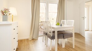 Een eethoek met een witte tafel en stoelen, een vaas met bloemen en een lamp.