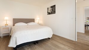 Een slaapkamer met een bed, twee nachtkastjes met lampen, een aan de muur hangend kunstwerk en een deur naar een andere kamer.