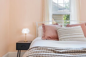 A bed with a white headboard, a bedside table with a lamp, and a window with curtains. - SpaciousStay- Game Room - NearClinic & UniversityCircle (Cleveland Heights)