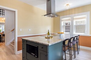 A kitchen with a central island, bar stools, a built-in oven, and a window with blinds. - SpaciousStay- Game Room - NearClinic & UniversityCircle (Cleveland Heights)