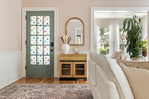 A room with a green door, a wooden cabinet, a mirror, and a large plant. - SpaciousStay- Game Room - NearClinic & UniversityCircle (Cleveland Heights)