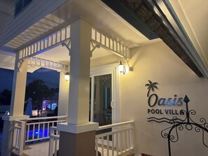 Ein überdachter Außenbereich mit Pool, weißer Brüstung und einem Schild mit der Aufschrift 'Oasis Pool Villa'.