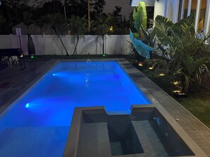 Ein rechteckiger Swimmingpool mit glasklarer, blauer Wasseroberfläche, umgeben von einer gefliesten Liegefläche und einer niedrigen Ziegelmauer.