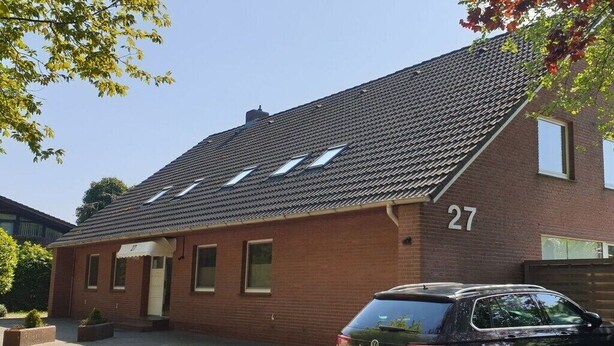 A two-story brick building with a sloped roof, numbered 27, and a parked car in front. - Vosshörn 27 - Apartment 1 (Cuxhaven-Duhnen)