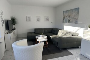 Ein modernes Wohnzimmer mit einer Eckcouch, einem weißen Sessel und einem kleinen Couchtisch.