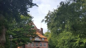 A traditional brick building with a central entrance, surrounded by dense greenery. - Vosshörn 27 - Apartment 1 (Cuxhaven-Duhnen)