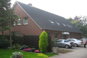 Ein zweigeschossiges Haus mit geneigtem Dach, einer Ziegel-Fassade und einem kleinen Vorgarten mit Blumen und einer hohen Konifer.