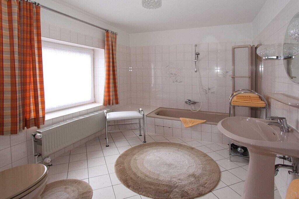 A bathroom with a bathtub, a sink, a toilet, and a window with curtains.