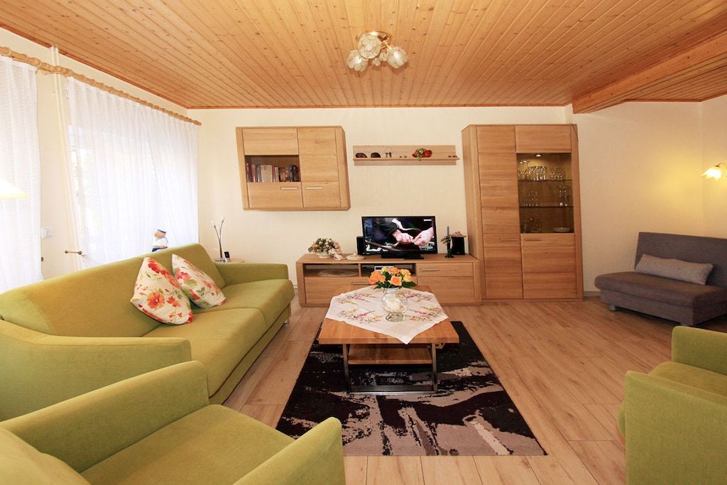 Un salon avec un canapé, une table basse ornée de fleurs, un téléviseur et des meubles en bois.