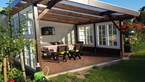 A covered patio with a table and chairs, a brick floor, and a view of a house with large windows. - Holiday apartment with 2 bedrooms (Gadendorf)