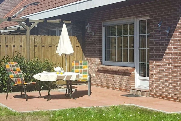 Eine Terrasse mit zwei Stühlen und einem Tisch, einem Holzzaun und einem Backsteinhaus mit einem Fenster.