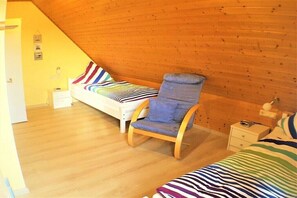 Une chambre avec deux lits, une chaise en bois, une table de chevet et une lampe fixée au mur.