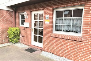 Ein rot backengebackenes Gebäude mit einer weißen Tür, einem Fenster mit Spitzenvorhängen und einem kleinen weißen Briefkasten.