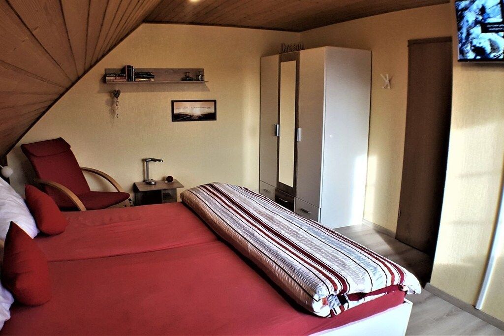 Ein Schlafzimmer mit einem Bett, einem Sessel, einem Kleiderschrank und einem Fernseher.