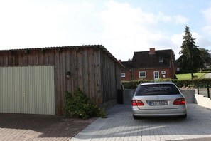 A car parked in front of a building with a garage door and a brick house in the background. - Holiday apartment with 1 bedroom (Gadendorf)
