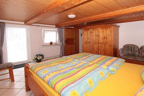 Une chambre avec un plafond en bois, un lit recouvert d’une courtepointe colorée, une fenêtre avec des rideaux et une armoire en bois.