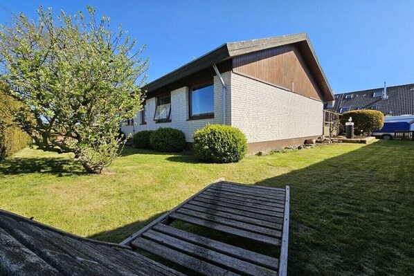 Ein eingeschossiges Haus mit einem geneigten Dach, einem kleinen Vorgarten und einer Holzterrasse.