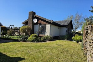 Ein einstöckiges Haus mit Backsteinkamin, einer Haustür und einem kleinen Vorgarten mit Rasen und Sträuchern.