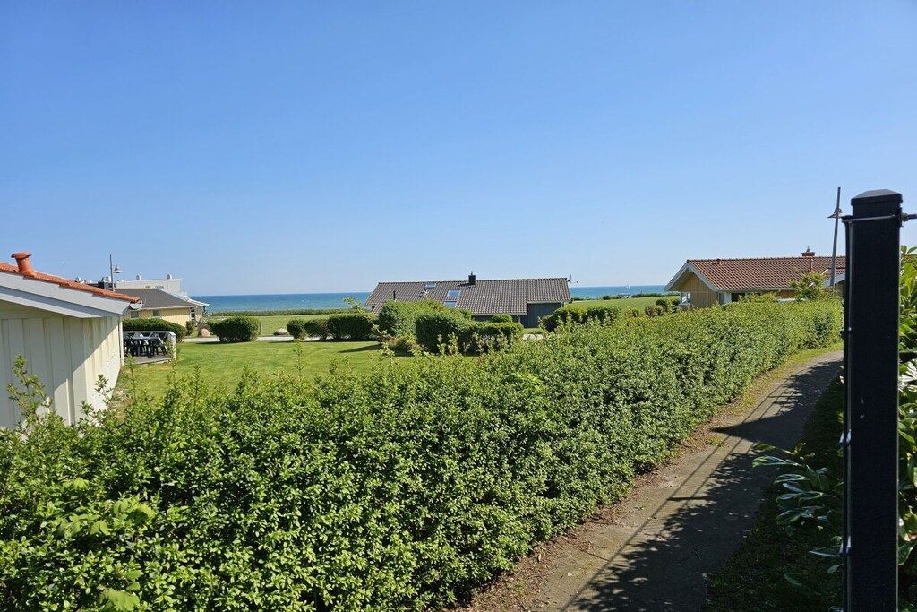A residential area with a pathway leading to a house with a tiled roof, surrounded by well-maintained greenery and a clear view of the sea.