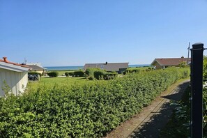 Un quartier résidentiel avec un sentier menant à une maison à toit de tuiles, entourée d’un jardin bien entretenu et offrant une vue dégagée sur la mer.