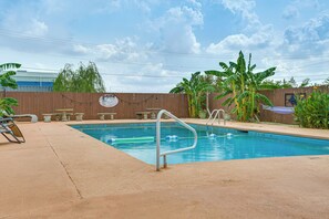 A swimming pool with a wooden deck, lounge chairs, and a fence with a sign.