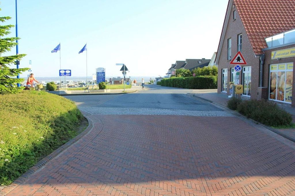 A paved pathway leading to a building with a red roof, a triangular warning sign, and flags.