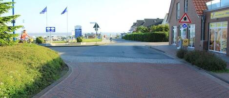 A paved pathway leading to a building with a red roof, a triangular warning sign, and flags.
