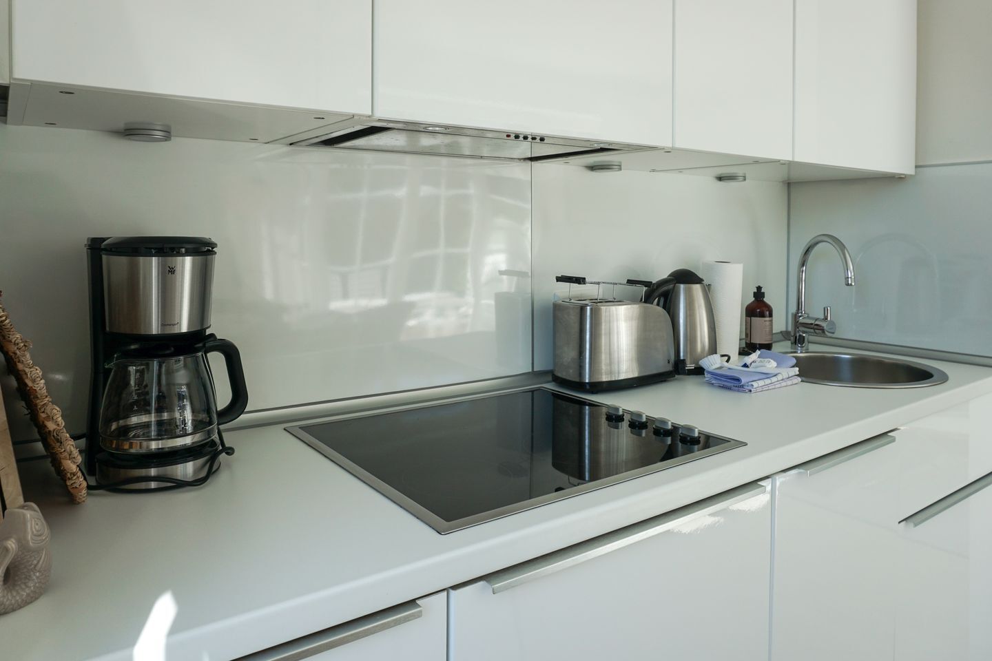 Una cocina moderna con placa vitrocerámica integrada, cafetera, hervidor y lavabo.