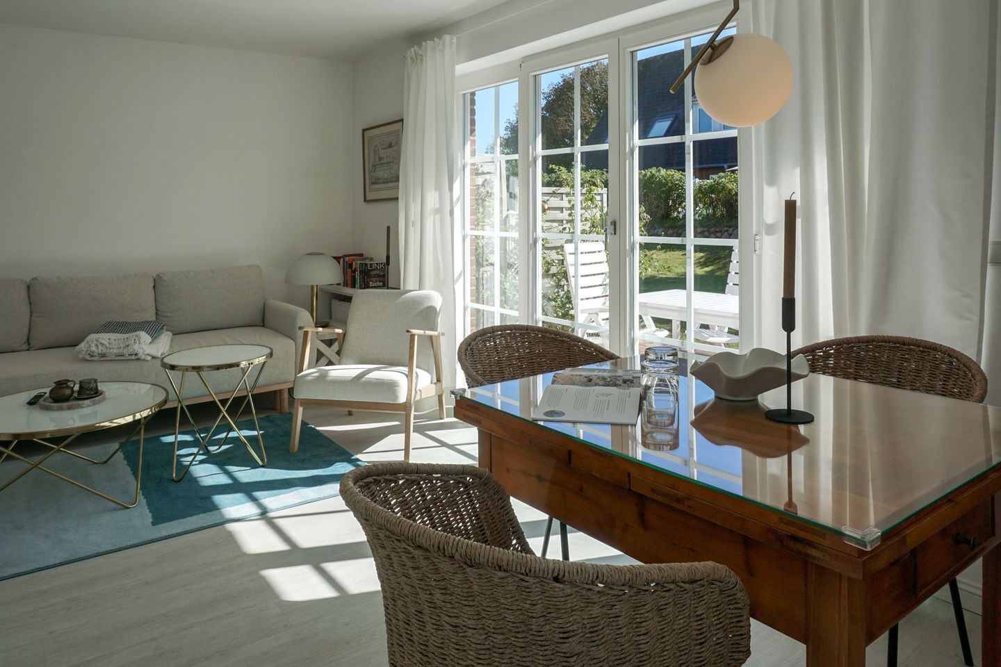 A living room with a sofa, two chairs, a glass-top dining table, and a view through large windows.
