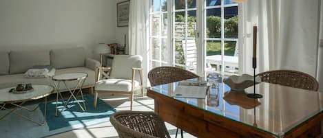 A living room with a sofa, two chairs, a glass-top dining table, and a view through large windows.