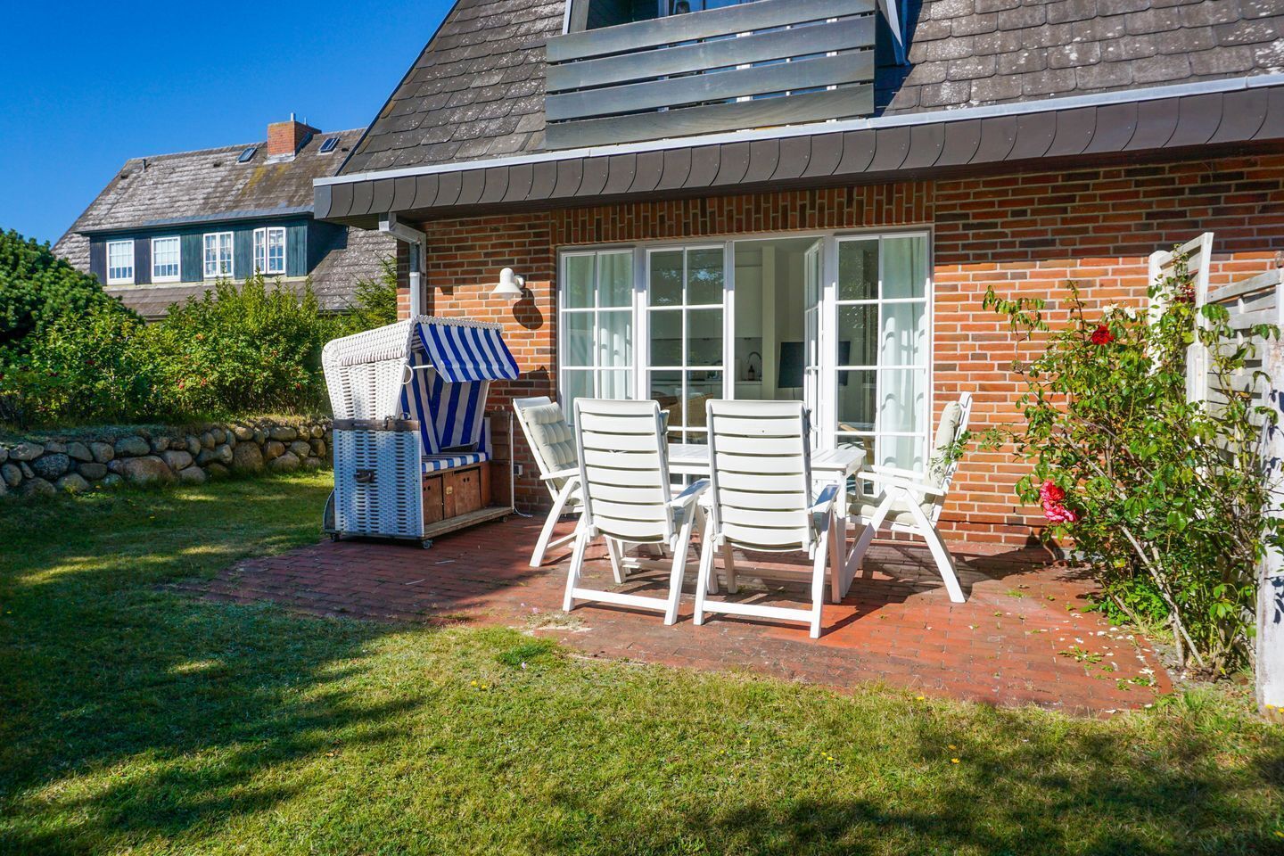 A brick house with a patio area featuring a table and chairs, a wicker chair, and a covered grill.
