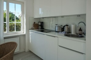 A modern kitchen with white cabinets, a stainless steel sink, and a window with a view of greenery. - Friesenring 17c - Cozy Vacation Rental at Friesenring 17c in Wenningstedt (Wenningstedt-Braderup (Sylt))